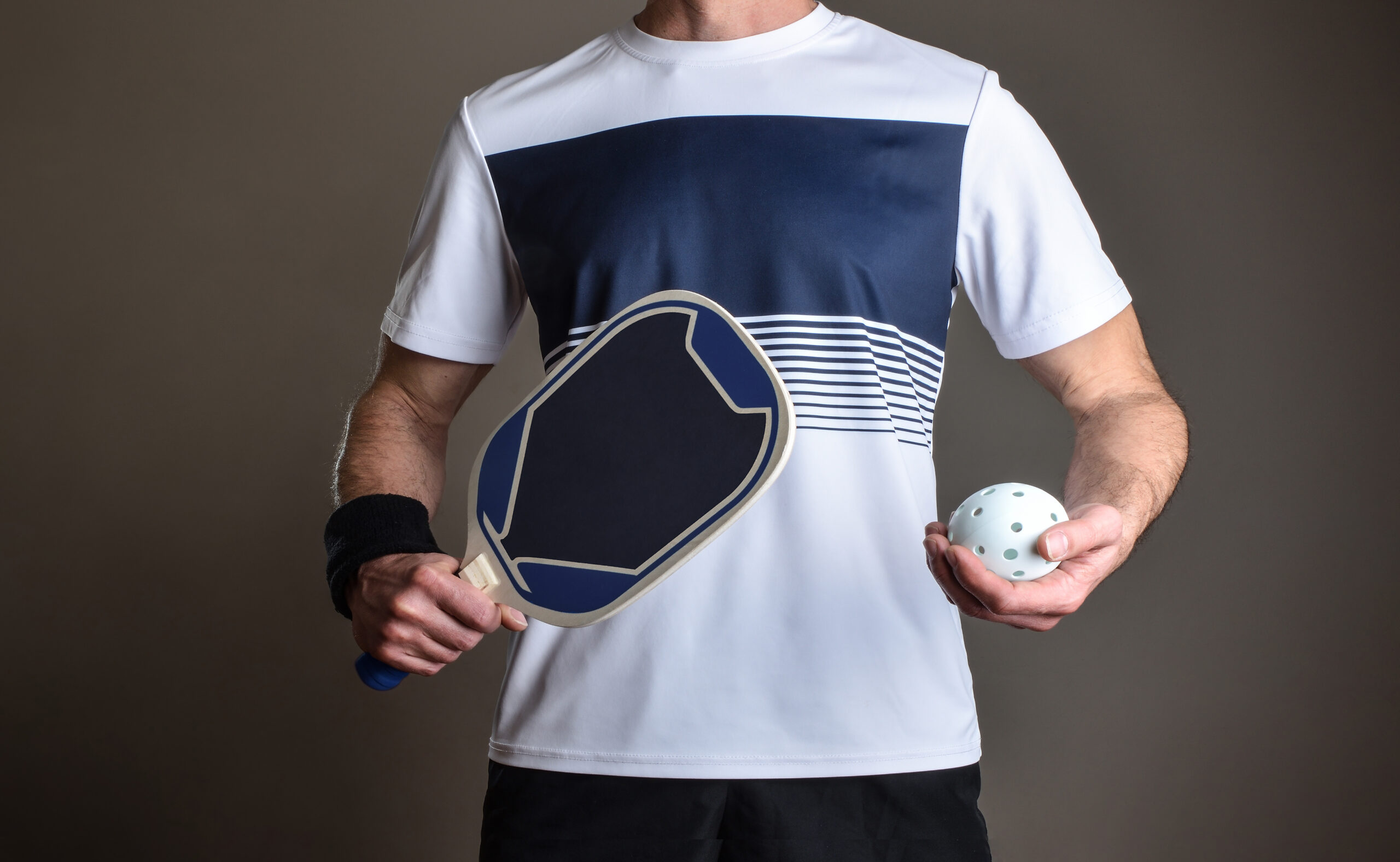Detail of pickleball player with sports clothing and racket and playing ball in hands on gray isolated background.